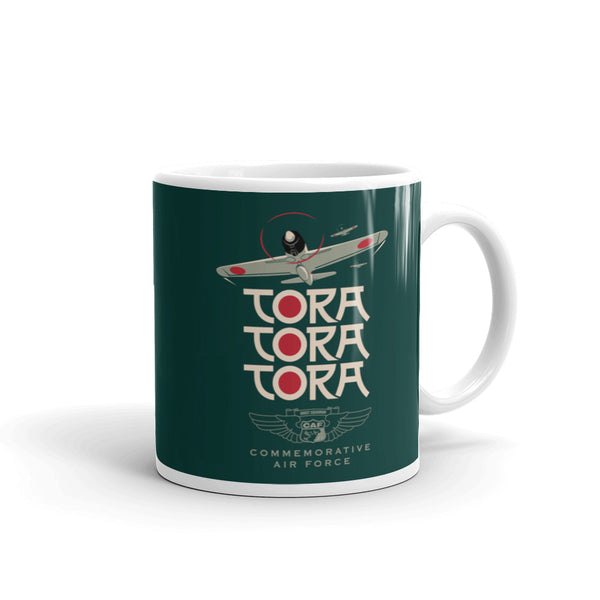 A ceramic mug with a green background featuring a graphic with the text 'TORA TORA TORA' and an illustration of an airplane.